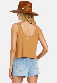 Brown ribbed tank top with a scoop back, paired with light blue denim shorts, featuring frayed hems and back pockets. Woven hat with a wide brim.