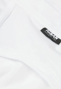 Weißes Baumwoll-T-Shirt, das eine weiche Stoffstruktur zeigt, gefaltet mit einem sichtbaren schwarzen Etikett, das "YUTAN, intimo, uomo" in der Nähe des Kragens liest.