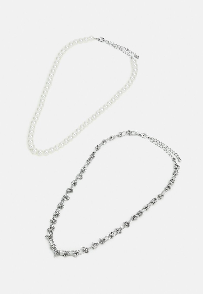 To halskæder: den ene med runde hvide perler, den anden i sølvmetal, med sammenkædede former og en lås med justerbar kæde.