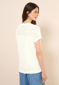 T-shirt de couleur claire avec un panneau en maille à l'arrière. Manches courtes, encolure ronde et tissu doux. Présente une coupe décontractée.