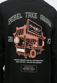 Hanorac negru pe spate cu un grafic al unui cărucior de mâncare ramen, text japonez și fraze despre programul de lucru și legume proaspete.