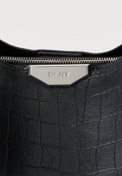 Близък план на черна текстурирана чанта DKNY със сребрист цип и метална табелка с марката.