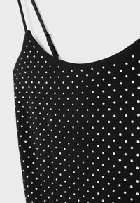 Czarny bezrękawnik uszyty z materiału, z kropkowym wzorem z małych srebrnych ćwieków równomiernie rozmieszczonych na powierzchni.