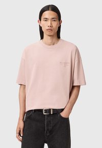 Jasnoróżowa, oversize koszulka z krótkimi rękawami i okrągłym dekoltem, z subtelnym logo na lewej piersi i gładką bawełnianą teksturą.