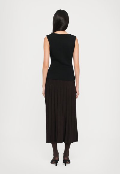 Black fitted sleeveless top with a scoop neckline, paired with a floor-length pleated dark brown skirt and black heeled shoes.