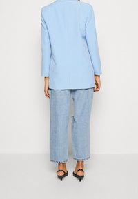 Ljusblå skräddarsydd kavaj med en enda slits, parat med ljusblå urtvättade vida jeans. Svarta sandaler med klack och remmar fulländar looken.