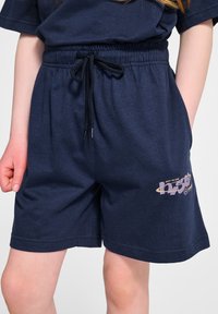 Marinblå bomullsshorts med resårmidja och dragsko, med en ljuslila grafisk design på vänster ben.