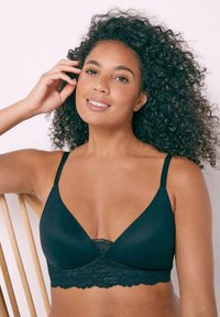 Mustan bralette, jossa on pitsireunus, kolmion muotoinen, ohuet säädettävät hihnat ja pehmeä kangas. Minimalistinen muotoilu.