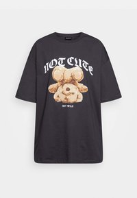 T-shirt oversize nera con grafica di un orso in stile cartoon e la scritta "NON CARINA MA SELVAGGIA" in lettere bianche in grassetto sul davanti.