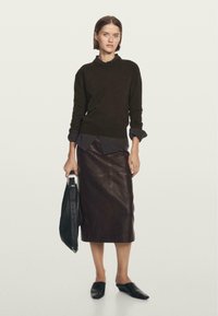 Maglione a maglia marrone scuro con collo alto, indossato sopra una camicia blu, abbinato a una gonna a matita in pelle marrone e mule nere. Borsa nera inclusa.