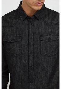 Tummanharmaa farkkupaita, jossa on napitettava etuosa, kaksi rintataskua ja kärjellinen kaulus, joka on tekstuuriltaan mielenkiintoinen.