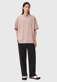 Helles rosa Baumwoll-T-Shirt mit lockerer Passform, Rundhals, kurzen Ärmeln und weißem aufgedrucktem Logo, kombiniert mit schwarzen lockeren Stoffhosen.