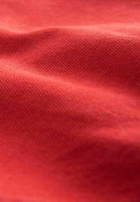 Röd texturerad tyg med subtila diagonala linjer, som visar en mjuk och slät yta samt små variationer i nyans.