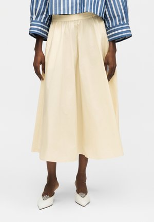 Tumea nahaga inimene, kes kannab kreemjat midi-seelikut, sinimustvalget triibulist pikkade varrukatega särki ja valgeid, pitsdetailidega teravate varvastega kontsakingi.