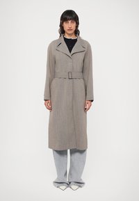 Szary płaszcz trench z wełny z paskiem, szerokimi klapami, długimi rękawami i prostym krojem, połączony z jasnym dżinsem oraz spiczastymi białymi butami.