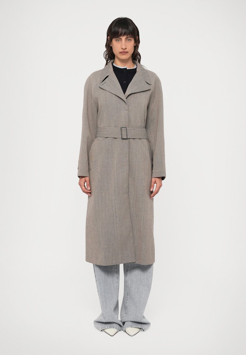 Szary płaszcz trench z wełny z paskiem, szerokimi klapami, długimi rękawami i prostym krojem, połączony z jasnym dżinsem oraz spiczastymi białymi butami.