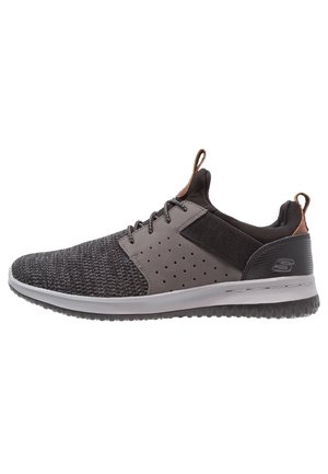 Zapatilla deportiva gris con parte superior de punto texturizado, paneles perforados, acentos negros y una suela acolchada. Presenta cordones y una lengüeta.