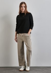 Schwarzes Langarmshirt, hellbeige maßgeschneiderte Hose und weiße Sneakers. Glatte Stoffqualität, lockere Passform, mit dezenten Nähten und Seitentaschen.