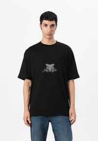 Black cotton t-shirt with a loose fit, featuring a silver graphic design on the chest. Short sleeves and a classic crew neckline.