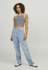 Prúžkovaný čierno-biely crop top spárovaný s svetlomodrými džínsy s vysokým pásom. Model má na sebe čierno-biele tenisky. Jednoduchý, príležitostný dizajn.