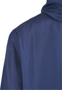 Veste bleu marine en tissu lisse et léger ; dotée d'une capuche, de détails cousus et d'un coupe décontractée. La vue arrière montre la texture du tissu.