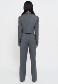 Grijze cropped blazer met gestructureerde schouders en lange uitlopende broeken. Getextureerde stof, met knoopdetails op de mouwen en een getailleerde taille.