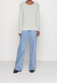 Helles graues Strickpullover mit langen Ärmeln und Rundhalsausschnitt, kombiniert mit hellblauen weiten Jeans. Glatte Textur, lässige Passform.