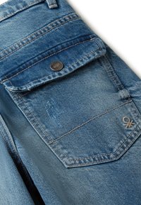 Pantalones vaqueros de denim azul con bolsillo trasero con solapa y botón de metal, ligeras degradaciones y pequeño logo bordado en la esquina inferior derecha.