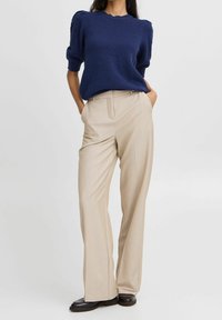 Námořnický pletený svetr s krátkým rukávem ve spojení s béžovými širokými kalhotami. Outfit doplňují tmavé boty.