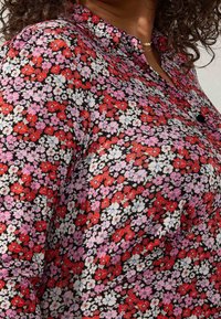 Blusa floreale caratterizzata da un mix di fiori rossi, rosa e bianchi su uno sfondo nero. Design con colletto e chiusura a bottoni, realizzata in tessuto leggero.