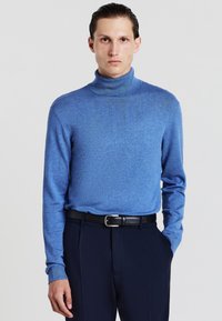 Blauer Rollkragenpullover aus weichem Strickstoff mit langen Ärmeln, kombiniert mit dunklen Hosen und einem schwarzen Gürtel, der eine glatte Textur aufweist.