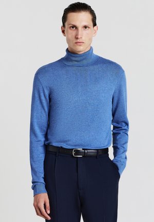 Pull à col roulé bleu en tricot doux avec des manches longues, associé à un pantalon sombre et une ceinture noire, présentant une texture lisse.
