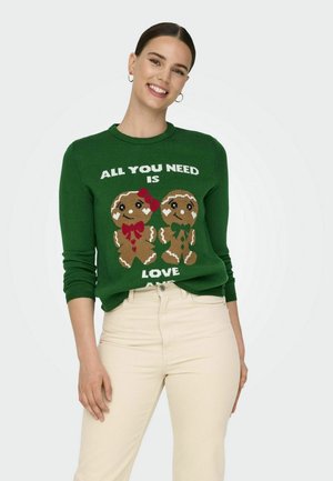 Suéter de punto verde con personajes de pan de jengibre que llevan lazos rojos y verdes, y el texto "TODO LO QUE NECESITAS ES AMOR" en blanco.