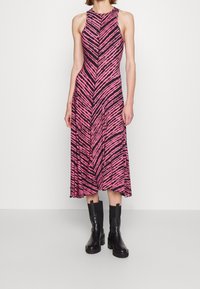 Sukienka bez rękawów o średniej długości w różowo-czarne paski, wykonana z lekkiego materiału. Połączona z czarnymi botkami za kostkę dla kontrastu.