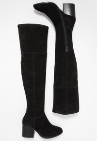 Botas negras hasta la rodilla hechas de ante, con un tacón de bloque, cremallera lateral y una textura suave con costuras decorativas en toda la superficie.