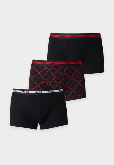 Trois boxers noirs pour hommes avec des ceintures élastiques, deux avec le logo rouge "HUGO" et un avec le logo blanc "HUGO" et un motif rouge.