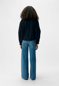 Blusa nera con maniche testurizzate, abbinata a jeans larghi di colore blu chiaro. Il tessuto appare liscio e il design presenta una vestibilità comoda.