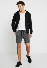 Felpa nera con zip, t-shirt bianca, pantaloni corti grigi, tutti in tessuto casual. Scarpe da ginnastica nere. Design semplice, senza motivi o loghi visibili.