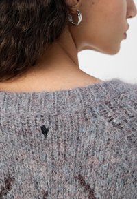Grauer gestrickter Pullover mit einer strukturierten, flauschigen Oberfläche und einem kleinen schwarzen Herzdetail auf der Rückseite. Zeigt ein lockeres, lässiges Design.