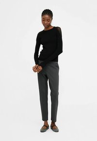 Černý svetr s dlouhým rukávem a krajkovým detailem na rameni, kombinovaný se šedými kalhotami na míru a plochými botami s texturovaným designem.