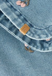 Vaaleansinistä farkkukangasta, jossa on vaaleanpunaisia ja ruskeita kirjailtuja kukkakuvioita sekä pieni ruskean nahkainen merkki, johon on ommeltu "LAF AUDREY".