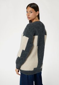 Maglione oversize con un motivo geometrico grigio scuro e crema. Realizzato in morbido materiale a maglia, presenta polsini e orlo a costine.