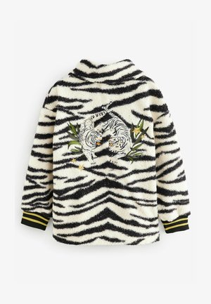 Valge fliisjakke mustade tiigri triipudega. Omab brodööritud tiigreid roheliste lehtede ja tähtede seas. Mustad mansetid kollaste triipudega.