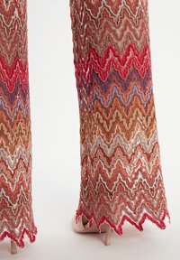 Pantalons en tricot avec un motif en zigzag dans des teintes de rouge, orange et bleu. L'ourlet est festonné, avec une texture en relief et des détails en dentelle.