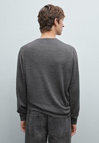 Gray long-sleeve sweater made of soft fabric, featuring a simple crew neck and relaxed fit, paired with dark gray jeans.