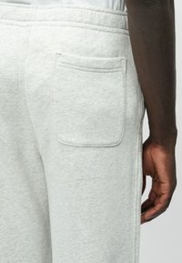 Joggers en gris claro confeccionados en un suave tejido cardado, con un bolsillo trasero y una cinturilla elástica. Los detalles de las costuras realzan el diseño.