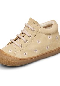 Beige semišová bota s vyšívanými květinovými vzory, béžovými tkaničkami a gumovou podrážkou. Kulatá špička a texturované detaily na podrážce.