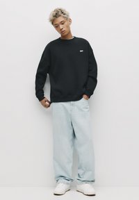 Sort bomulds sweatshirt med rund hals, løstsiddende pasform og logo-detalje. Lyseblå vide jeans parret med hvide sneakers.