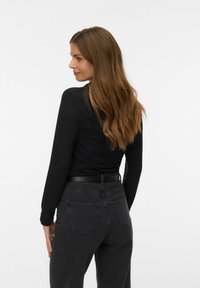 Črn dolg rokav vrh, v kombinaciji s temno sivo jeans. Vrh ima prilegajoč silhueto, medtem ko hlače vključujejo klasično zasnovo petih žepov.