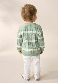 Mint green knitted sweater with white stripes, featuring a textured cable pattern. Paired with white pants and sneakers.